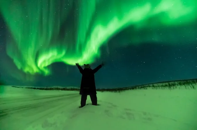 A person with arms raised under swirling green aurora on a snowy field