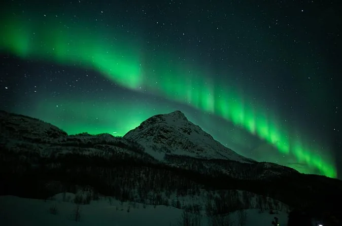 A green aurora arc over a snowy mountain at night